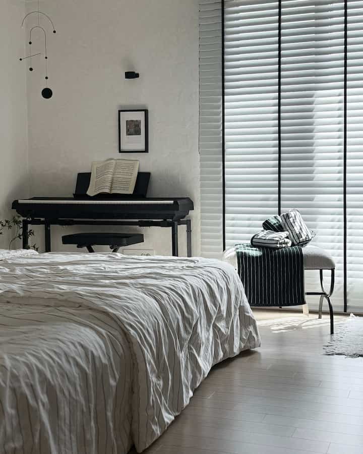 白と黒のモダンな寝室、ブラインドとピアノ、モビールが配置された印象的な空間