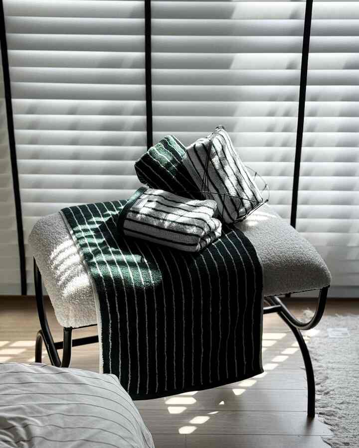 白と緑のトーンの寝室、スツールの上にストライプ柄のタオルセットが置かれた、清潔感のあるモダンな雰囲気のインテリア