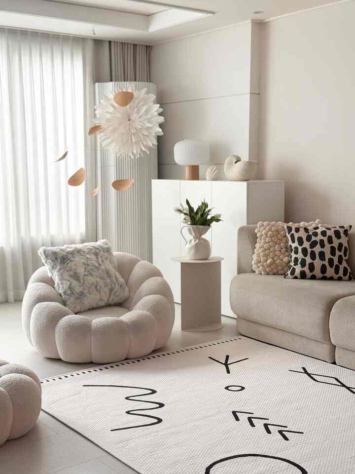 白とベージュのトーンが調和したリビング、曲線的なアームチェアとソファ、ラグが配置された雰囲気のある空間