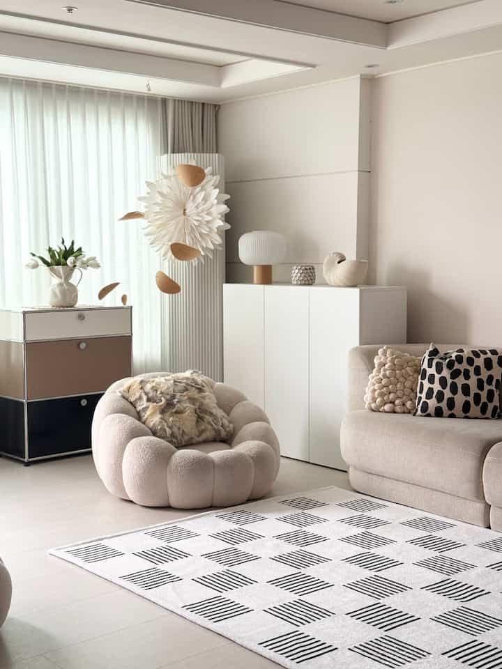 ベージュと白のトーンのリビング、丸いスツールとソファが配置されたナチュラルモダンな印象の空間