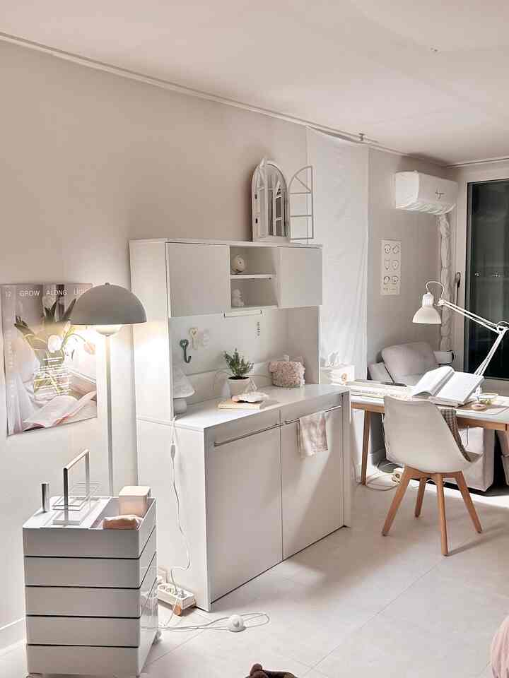 白とナチュラルトーンのワンルーム寝室兼作業スペース、収納棚とデスクが調和した印象的な空間