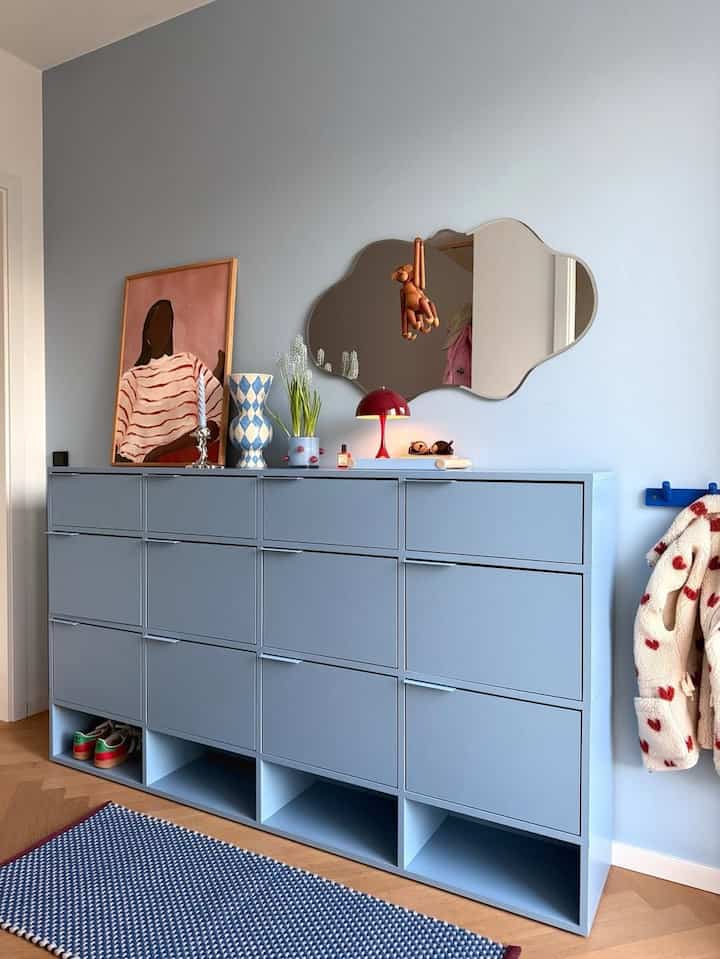 Powder blue wall living room featuring large multi-drawer cabinet, cloud-shaped wall mirror, and retro table lamp with clean modern vibe