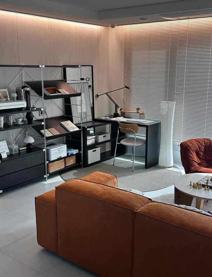 茶色のソファとモダンなホームオフィス、整頓された収納棚と照明が配置されたリビングスペース