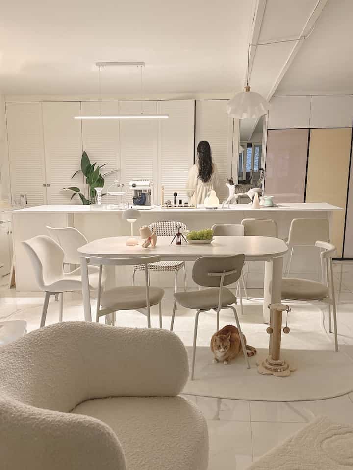 明るいホワイトトーンのキッチン兼ダイニング空間。セラミックテーブル、チェア、照明、そして2匹の猫がいる雰囲気のあるインテリア