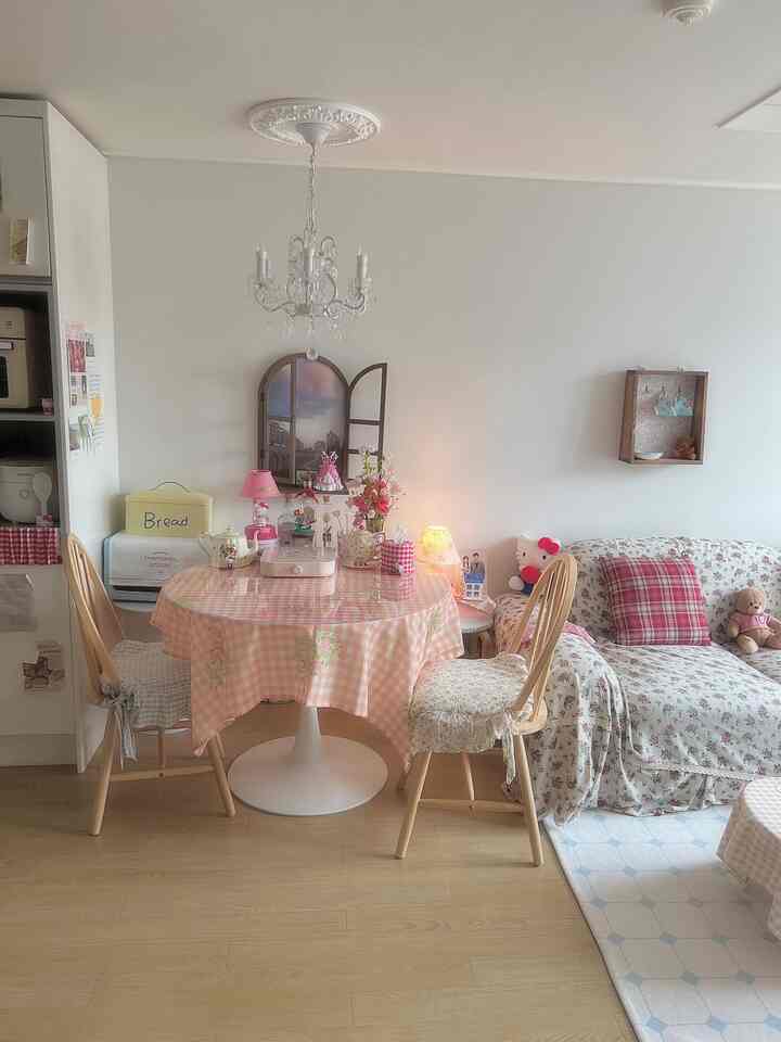 ピンクと白のトーンが印象的なかわいらしいダイニングルーム、シャンデリアと花柄のソファ、ギンガムチェックのテーブルクロスがアクセントの雰囲気あるインテリア