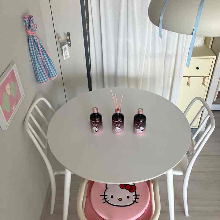ホワイトとピンクのトーンのキッチン、円形のダイニングテーブルとピンクのハローキティチェア、中央にディフューザーが配置された印象的で清潔感のあるインテリア
