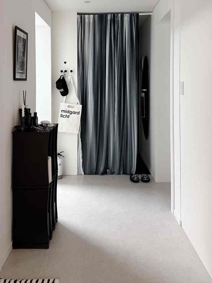白い壁と床の狭い玄関、黒いカーテンと収納棚が配置された印象的な空間