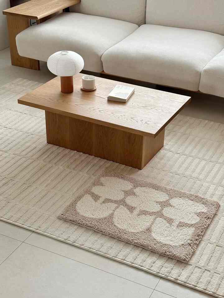ベージュ調のラグとかわいいバスマットが配置されたナチュラルモダンなリビング、木製のコーヒーテーブルと白いソファが落ち着いた雰囲気を演出している