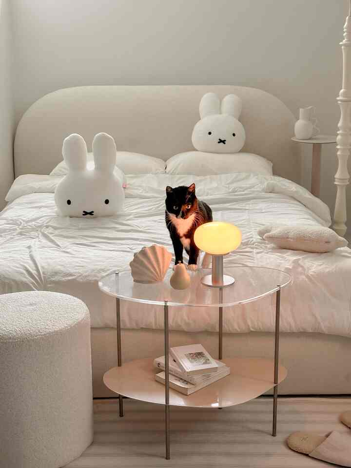 ホワイトとベージュのトーンの寝室、中央に透明なアクリルテーブルと猫が配置された落ち着いたミニマルな雰囲気のインテリア