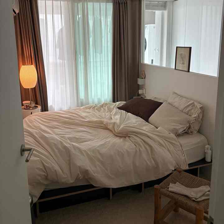 Soft white and brown toned bedroom featuring a single bed with pillows and cushions, warm lighting creating a cozy atmosphere