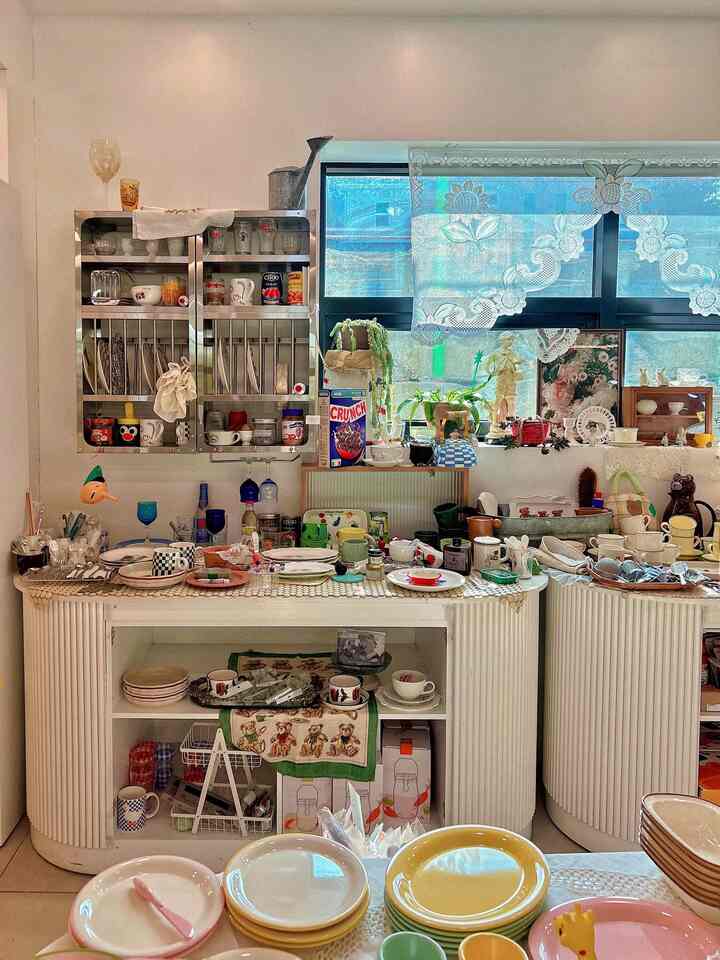 明るいホワイトトーンの壁とヴィンテージ皿やボウルが並ぶキッチン小物ショップの雰囲気のあるインテリア