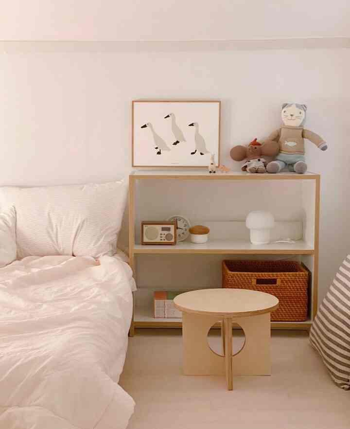 柔らかいナチュラルカラーの子供部屋、木製収納棚と丸いテーブル、赤ちゃんのおもちゃが置かれたシンプルなインテリア