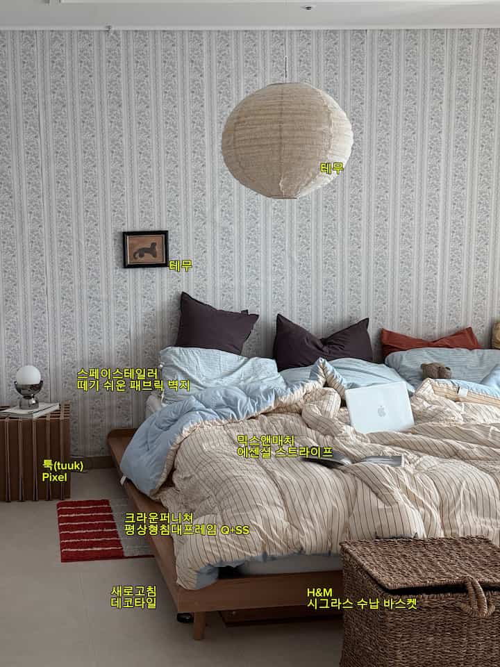 木目調とスカイブルーの寝室、ヘッドボード横にサイドテーブルとラタン収納バスケットが配置されたシンプルモダンなインテリア