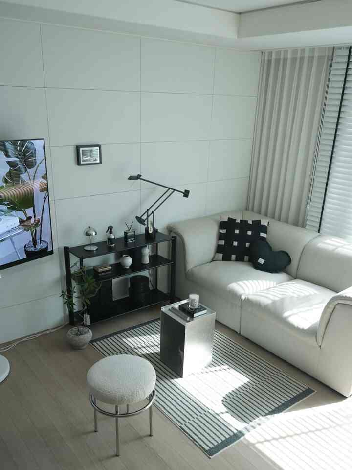 ホワイトとブラックのモノトーンのリビングルーム、ベージュのソファと黒いメタルラック、ブークレスツールと小さなナイトテーブルが配置されたモダンな雰囲気のインテリア