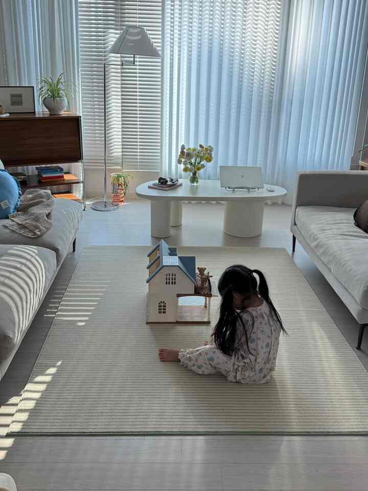 明るい白を基調としたリビング、ベージュのソファとラグ、中央にコーヒーテーブルと静かに遊ぶ子供がいる空間