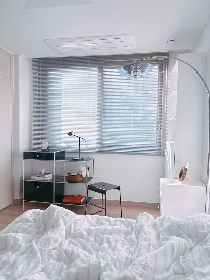 Bright and clean white-toned bedroom featuring metal furniture, blinds, and floor lamp in a modern, minimal style