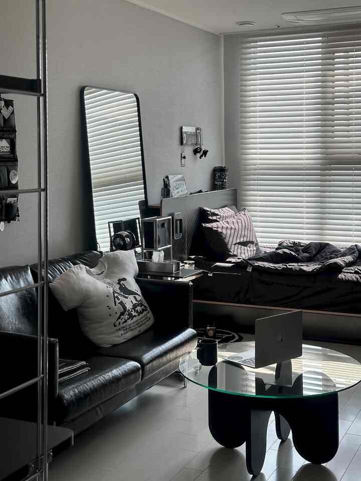 ブラックとホワイトのトーンのモダンなリビング、レザーソファとガラスのコーヒーテーブル、大きなブラインド付き窓が調和する空間