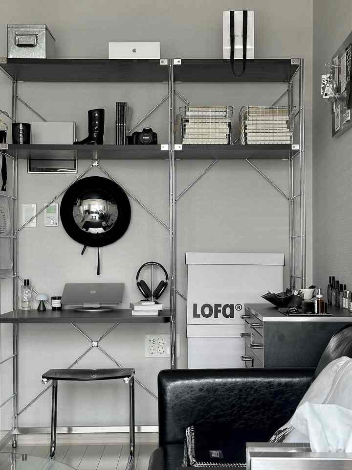 ブラックとホワイトのトーンのホームオフィス兼リビングルーム空間、メタルシェルフとスツール、ノートパソコンとヘッドフォンが配置されたシンプルでミニマルなインテリア