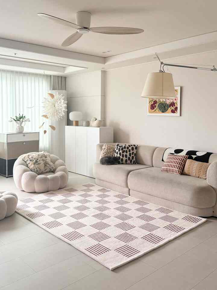 ホワイトとベージュのトーンのリビングルーム、モダンなソファと柄クッション、大きなラグが配置された雰囲気のある空間