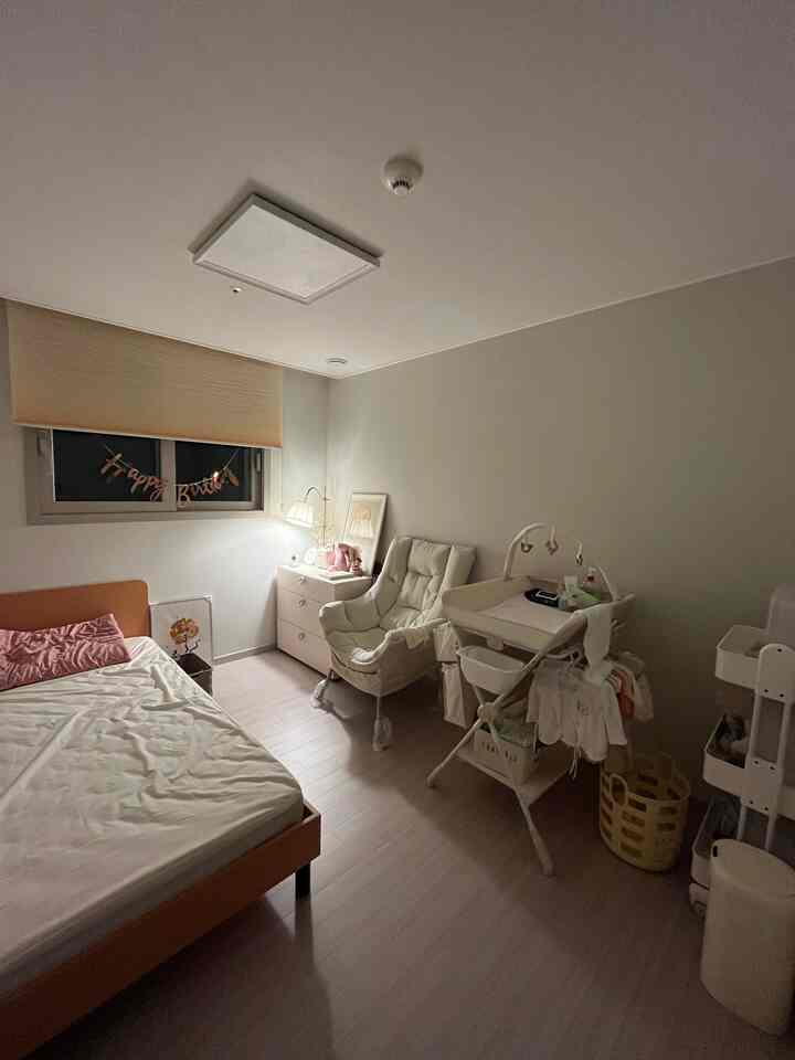 ベージュ調の寝室兼子供部屋、ナイトテーブルとアームチェア、オムツ交換台が配置された落ち着いた雰囲気のインテリア