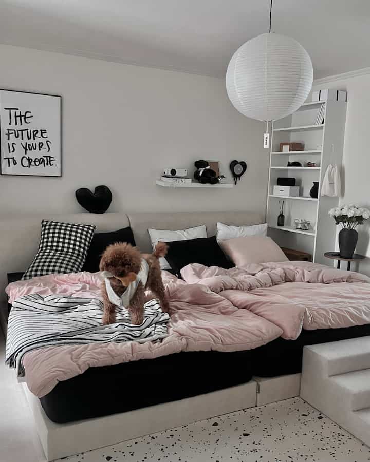 ピンクの寝具と黒いクッションが調和したモノトーンの寝室、ツインベッドとペット用ステップが配置された居心地の良い空間