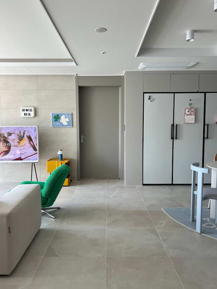 グレー調のリビングとキッチンの境界空間、淡いベージュのソファと緑のアームチェアが配された自然でモダンなインテリア