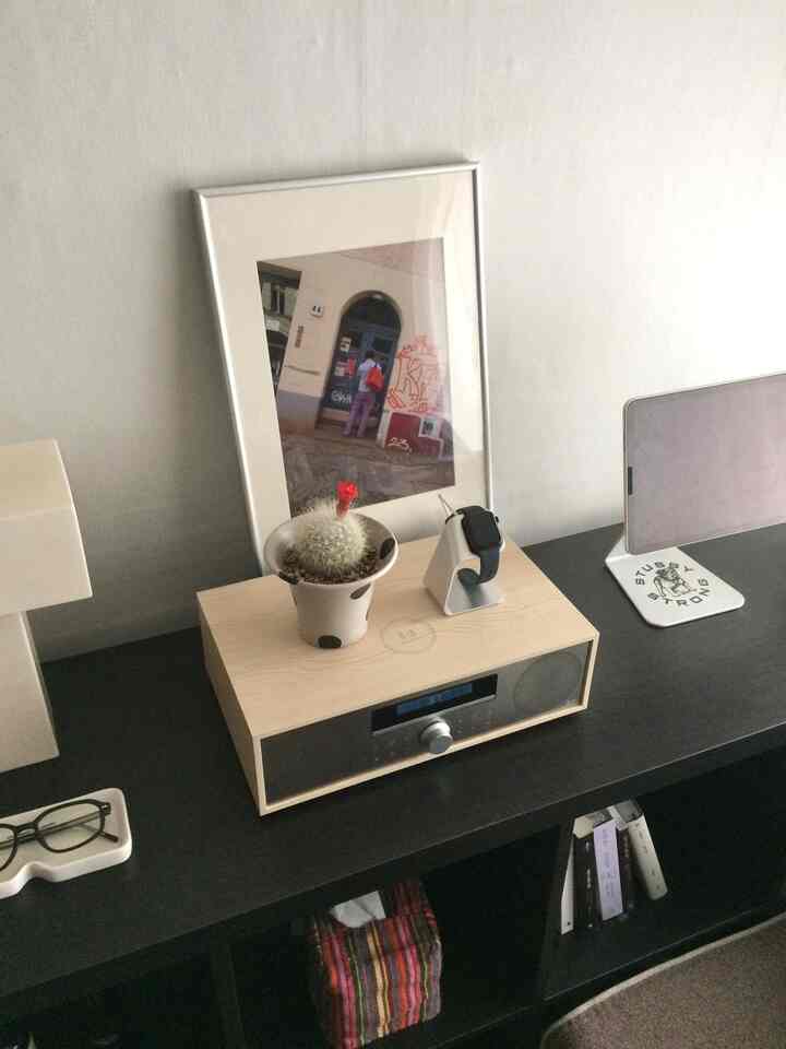 ベージュの壁と黒いサイドボードに自然な色調のラジオ、小さなサボテン、アップルウォッチスタンドが配置されたシンプルな空間