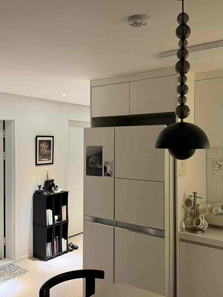 白と黒のトーンのキッチンスペース、ペンダントライトと本棚が配置されたミニマルでコンパクトな雰囲気のあるインテリア
