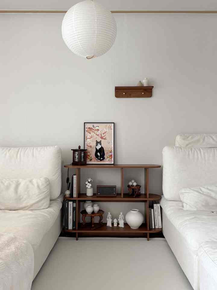 白とウォールナットの色合いのリビングルーム、二つのソファ間にウォールナットの棚とオブジェが配置されたシンプルで自然な雰囲気のインテリア