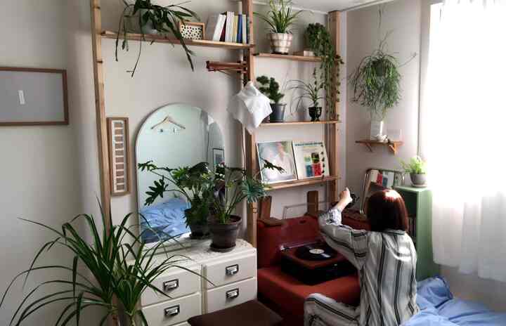 ナチュラルな木目調と白を基調とした小さなリビング、植物が豊富に配置された無加工の棚とレトロなLPターンテーブルのある空間