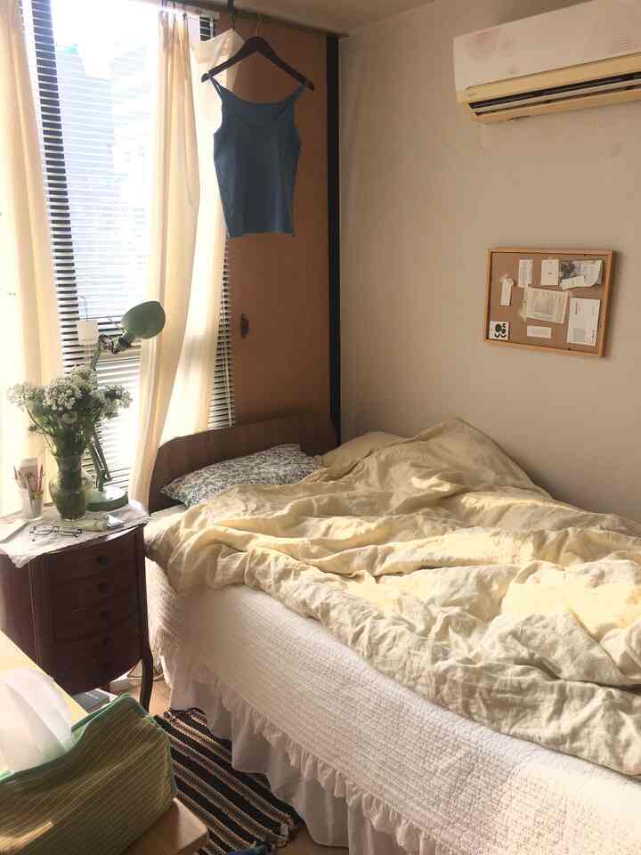 柔らかいイエローとホワイトの色調の寝室、ヴィンテージ風のナイトテーブルとアルミブラインドが温かい日差しを取り込む雰囲気のあるインテリア