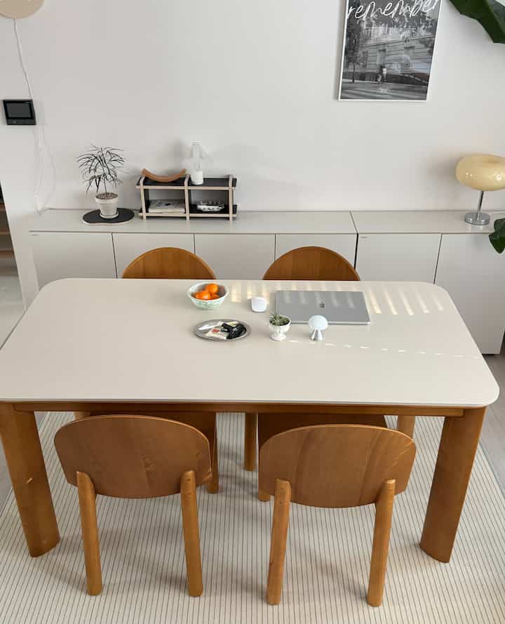 白と茶色の色調のリビングダイニング、4脚の木製椅子とシンプルな収納キャビネットが配置されたミニマルで自然な印象のインテリア