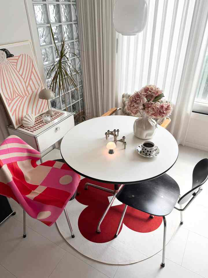 白と赤のトーンのダイニングルーム、丸いダイニングテーブルと2脚の椅子、花瓶と照明が配置された雰囲気のある空間