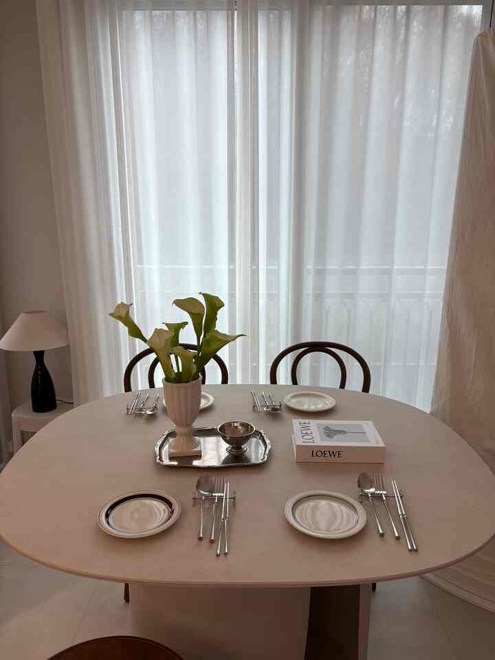 ベージュとホワイトの色調のリビングルーム、楕円形のテーブルに皿とカトラリーが並べられた雰囲気のあるフレンチカントリースタイルのインテリア