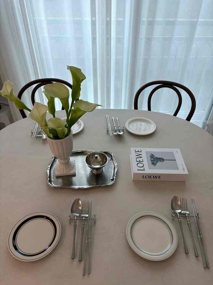 白と茶色のトーンのダイニング、木製の椅子と洗練された食器が配置された清潔感のある空間