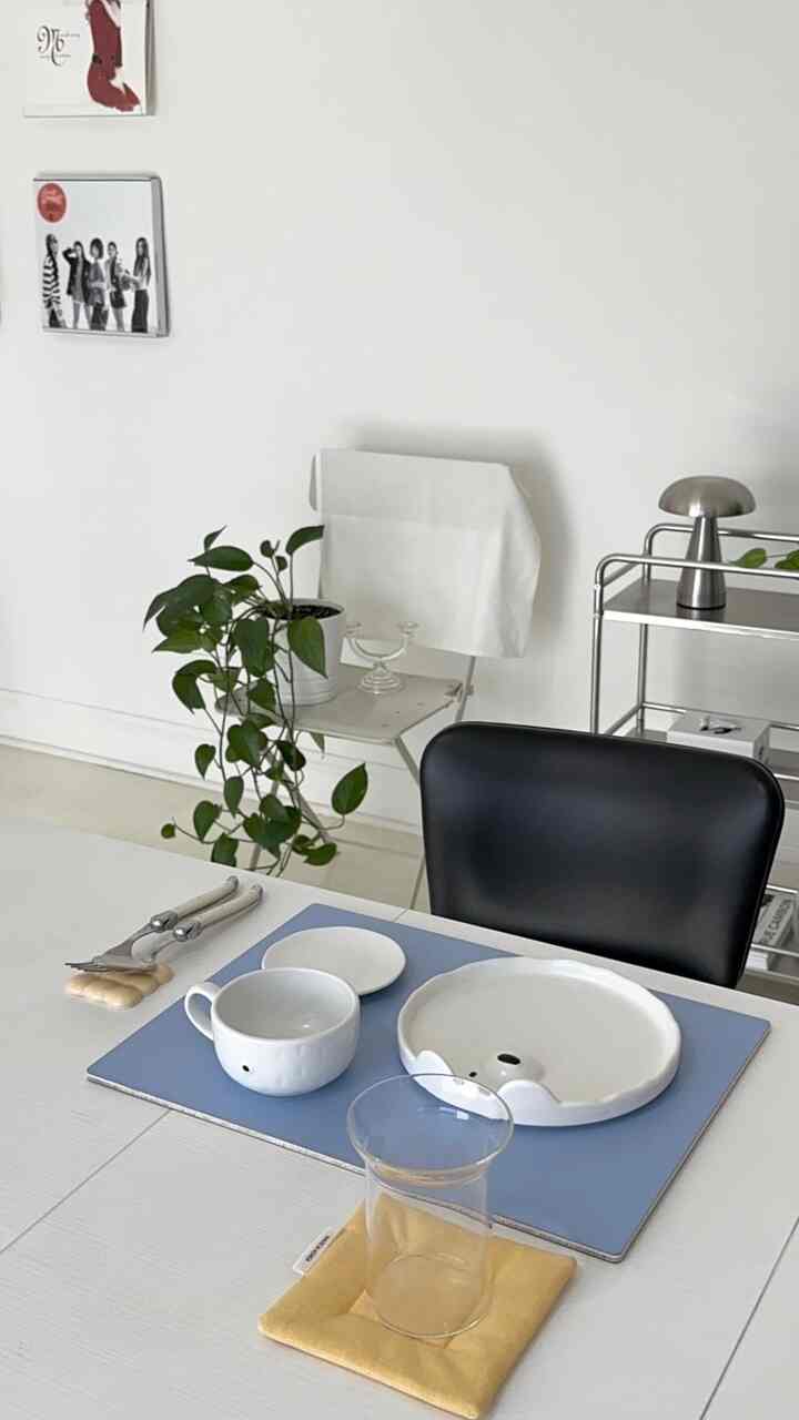 White-toned dining room featuring a dining table with cutlery and glassware, complemented by a green plant for a clean and cozy atmosphere