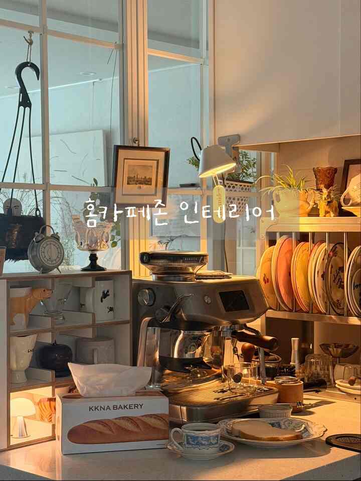 暖かいベージュの色調のキッチンおうちカフェ、キッチンアイランドにコーヒーマシンとヴィンテージカップが配置された雰囲気のある空間