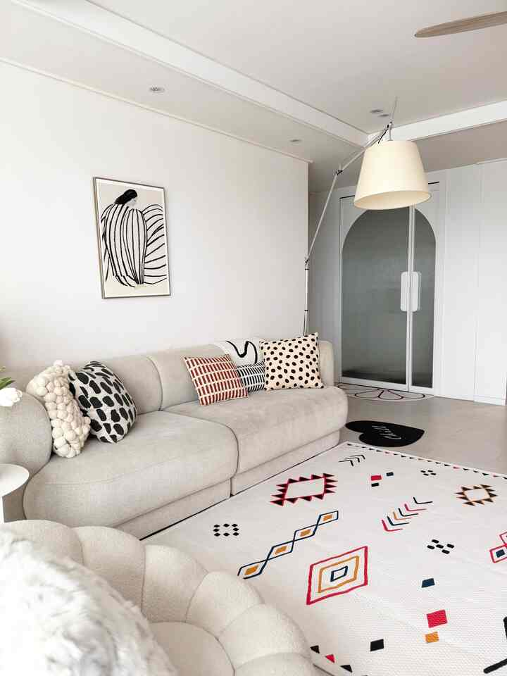 ホワイトとベージュの色調のリビング、大型ソファと模様のあるラグが配置されたモダンでナチュラルな雰囲気の空間