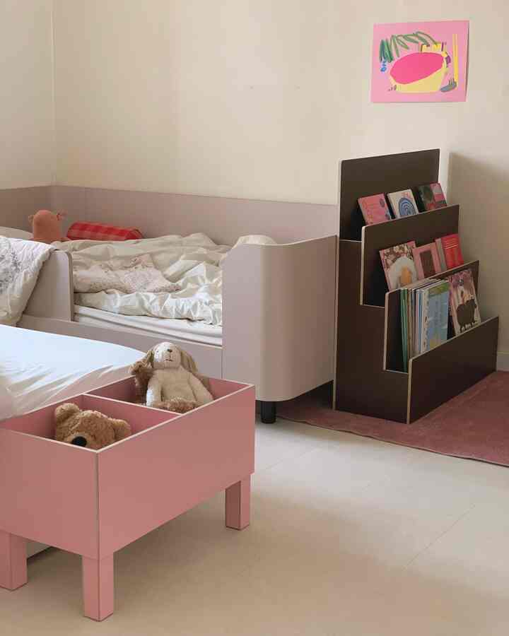 ピンクとベージュの色調の子供部屋、ベビーベッドと本棚、おもちゃ収納が整った雰囲気のあるインテリア