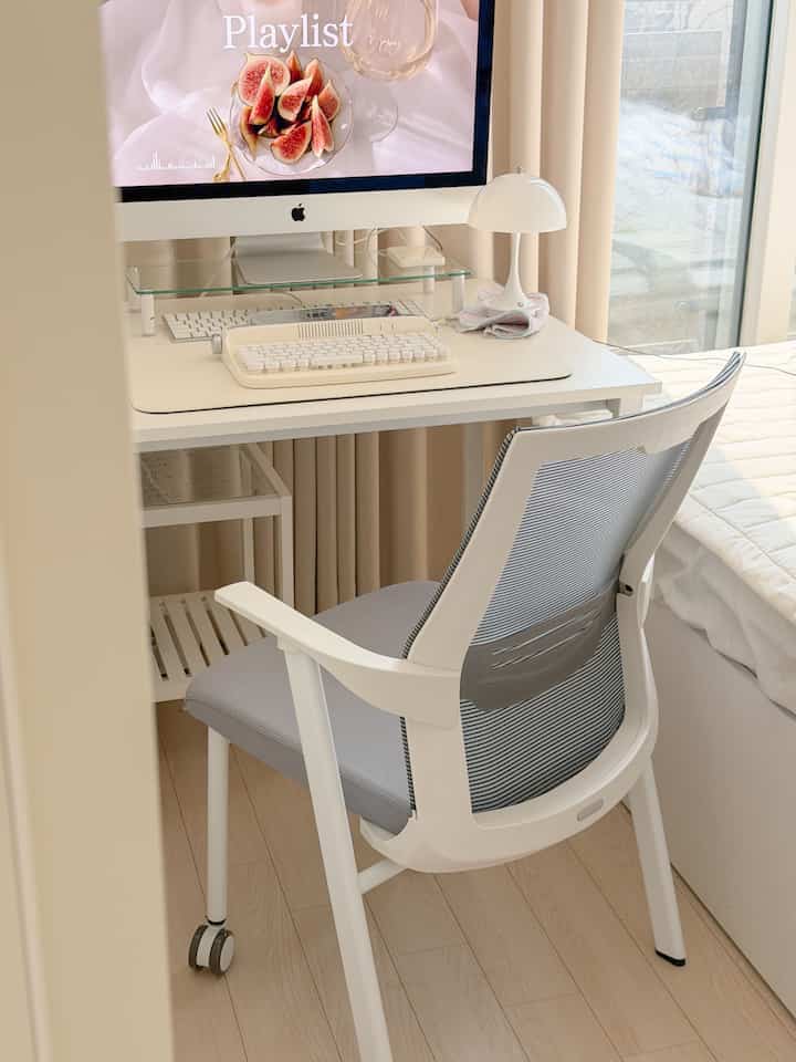 白とライトブラウンのトーンのコンパクトな寝室兼ホームオフィス、窓辺に配置されたデスクとオフィスチェアが置かれたシンプルな空間