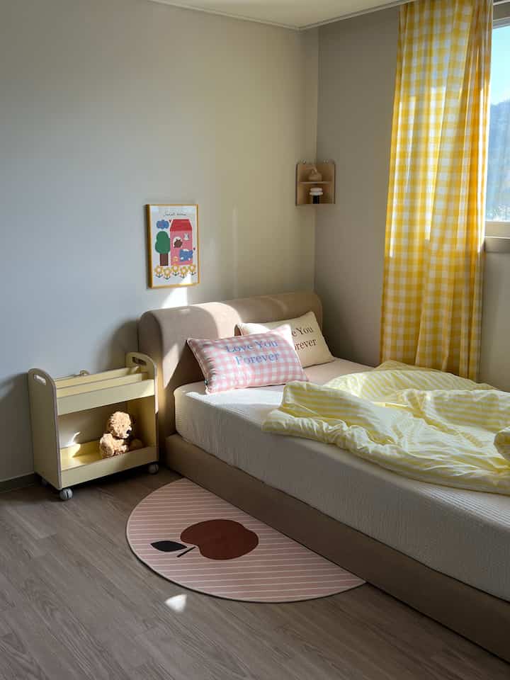 黄色とナチュラルカラーの子供部屋、ベッドとかわいいポスター、半円形のラグが配置された明るく居心地の良いインテリア