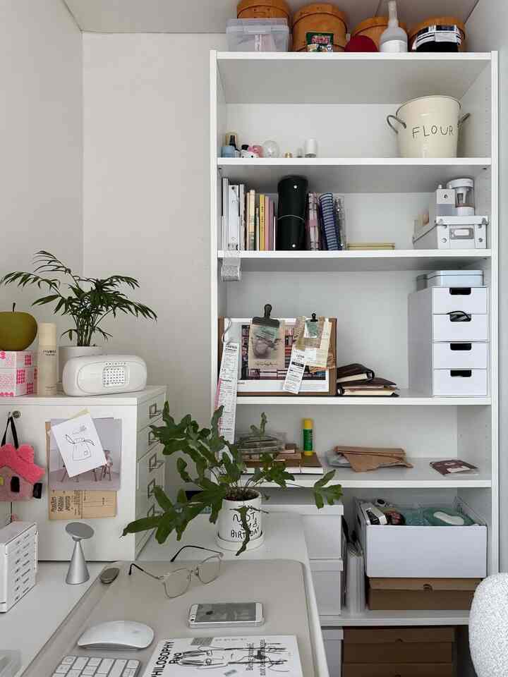 ホワイトカラーの書斎、整理された本棚とデスクにナチュラルなグリーンプラントが配置された、落ち着いた作業空間。