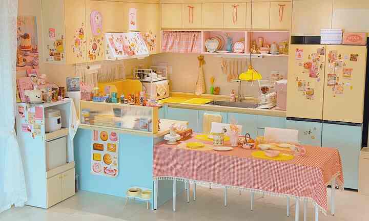 黄色とピンクの色調のキッチン、かわいい小物やキャビネット、ダイニングテーブルが配置されたラブリーキッチュスタイルの空間
