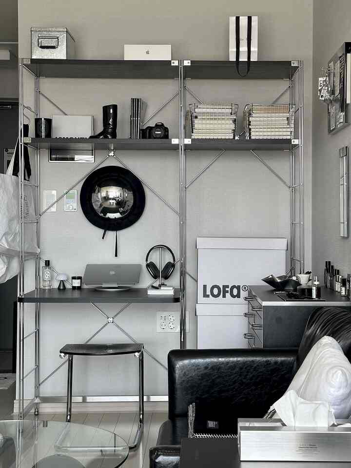 ブラックとシルバーのトーンが特徴のホームオフィス兼リビング、金属製シェルフと黒革ソファ、スツールが配置された印象的なインテリア