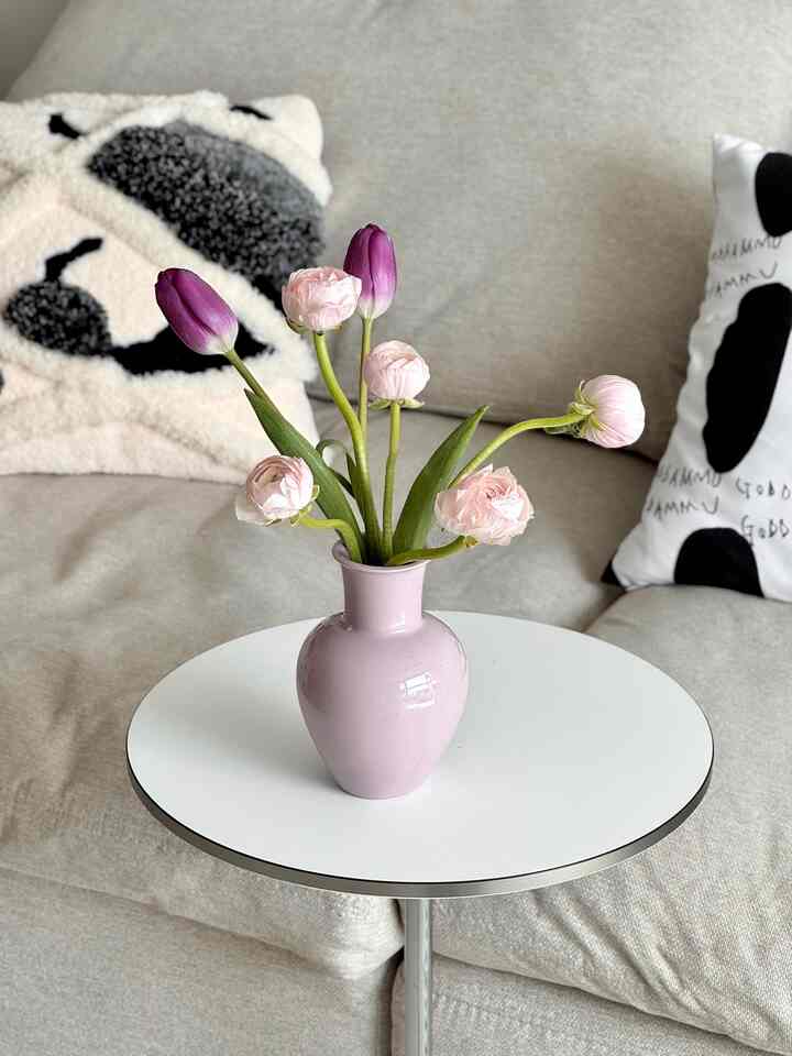 ベージュトーンのリビング、ベージュのソファと白いコーヒーテーブルの上にピンクの花瓶と花が配置された雰囲気のある空間