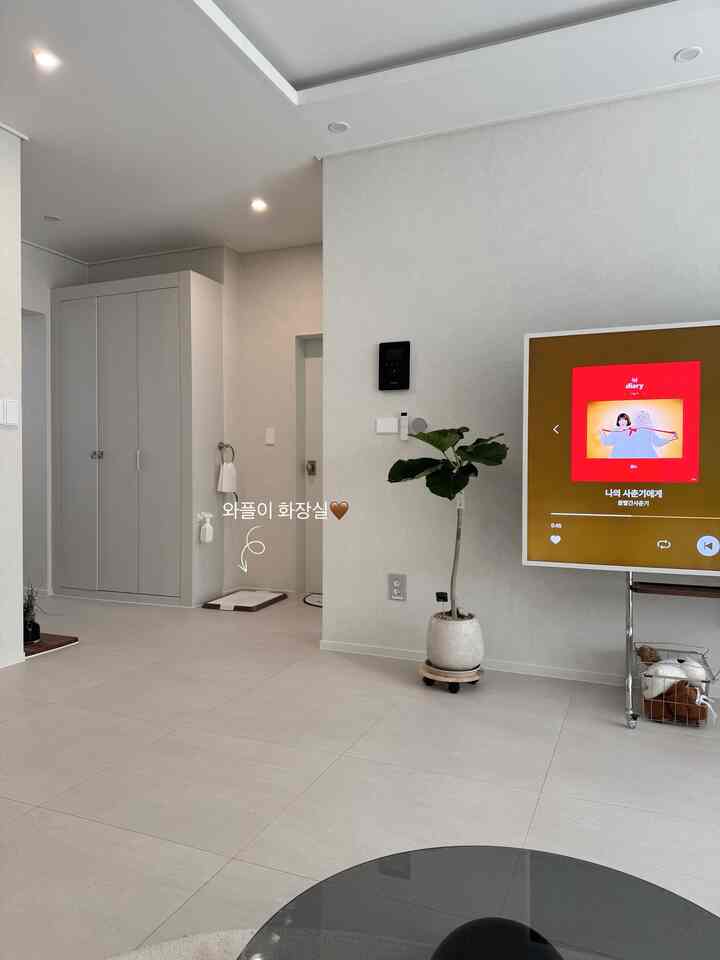 明るいホワイトトーンのリビング、テレビ台と大型キャビネット、植物とペット用品が配置された清潔感のある空間