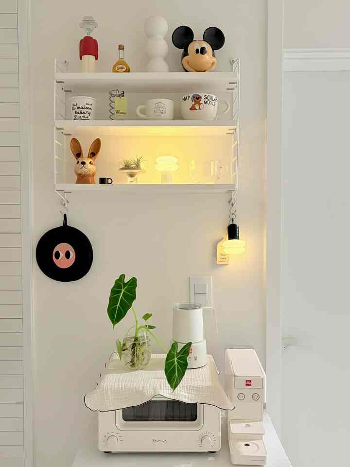 白とナチュラルカラーのキッチン、ストリングシェルフと小型家電、植物が配置された雰囲気のあるインテリア