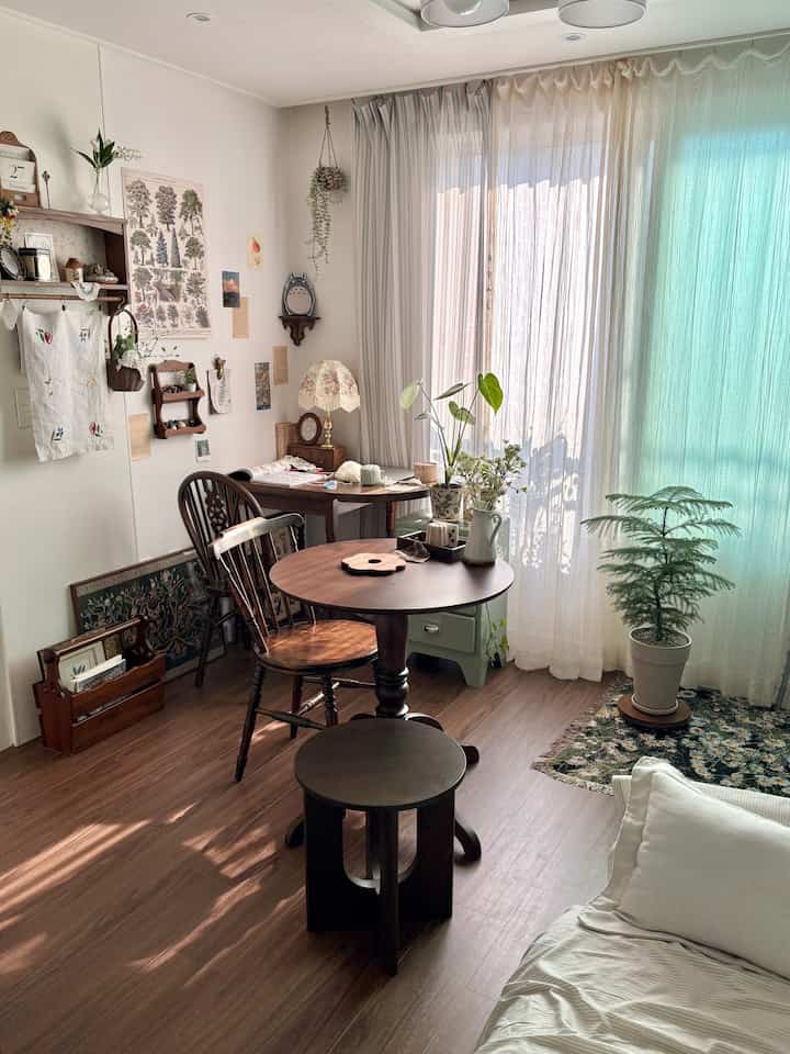白と茶色のトーンのダイニングルーム、ヴィンテージ家具と多様な植物が配置された雰囲気のある空間