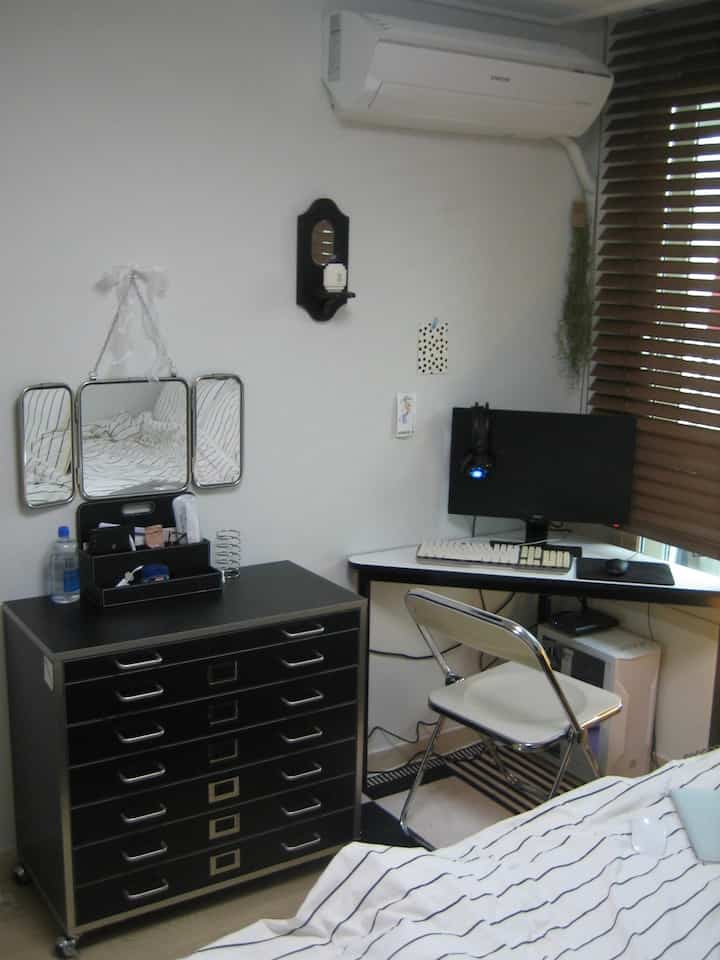 白と黒、木目調が調和した狭くてコンパクトな寝室、実用的なデスク、チェスト、三面鏡の化粧台が配置された空間