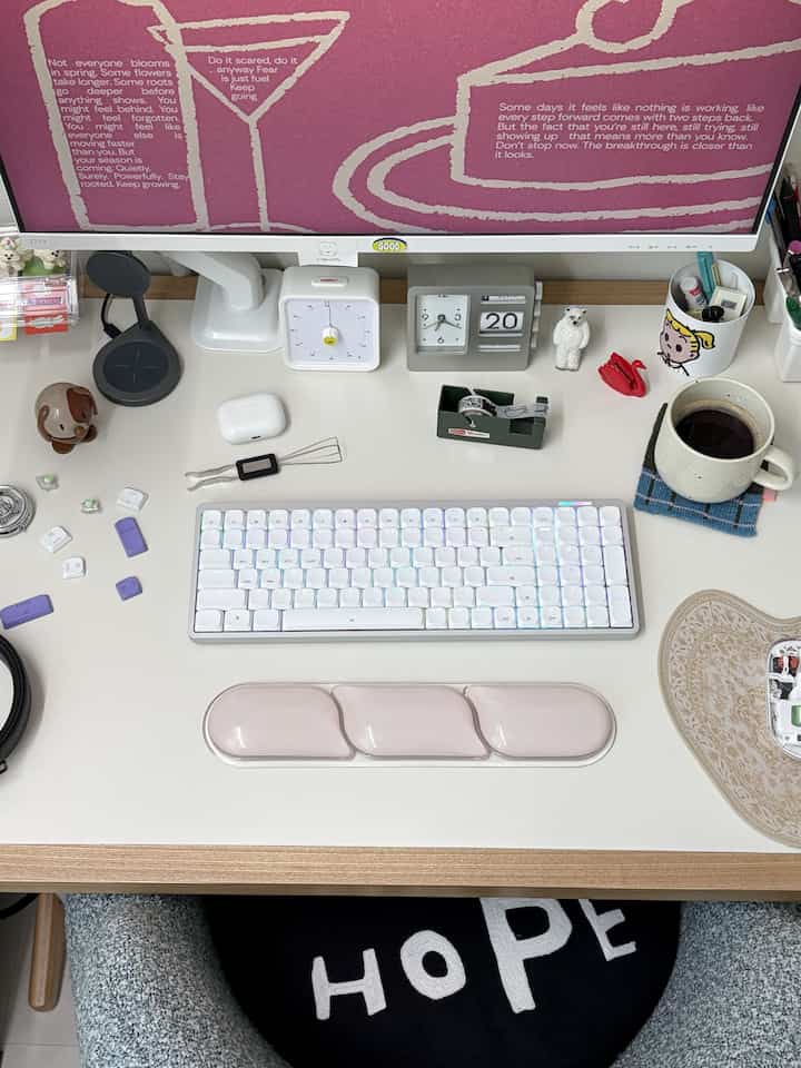 白とピンクのトーンのホームオフィスデスク、キーボードとモニタースタンドが整然と配置されたシンプルな作業空間